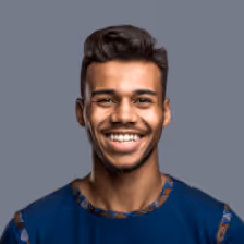 Smiling young man with short curly hair wearing a blue patterned shirt against a gray background.